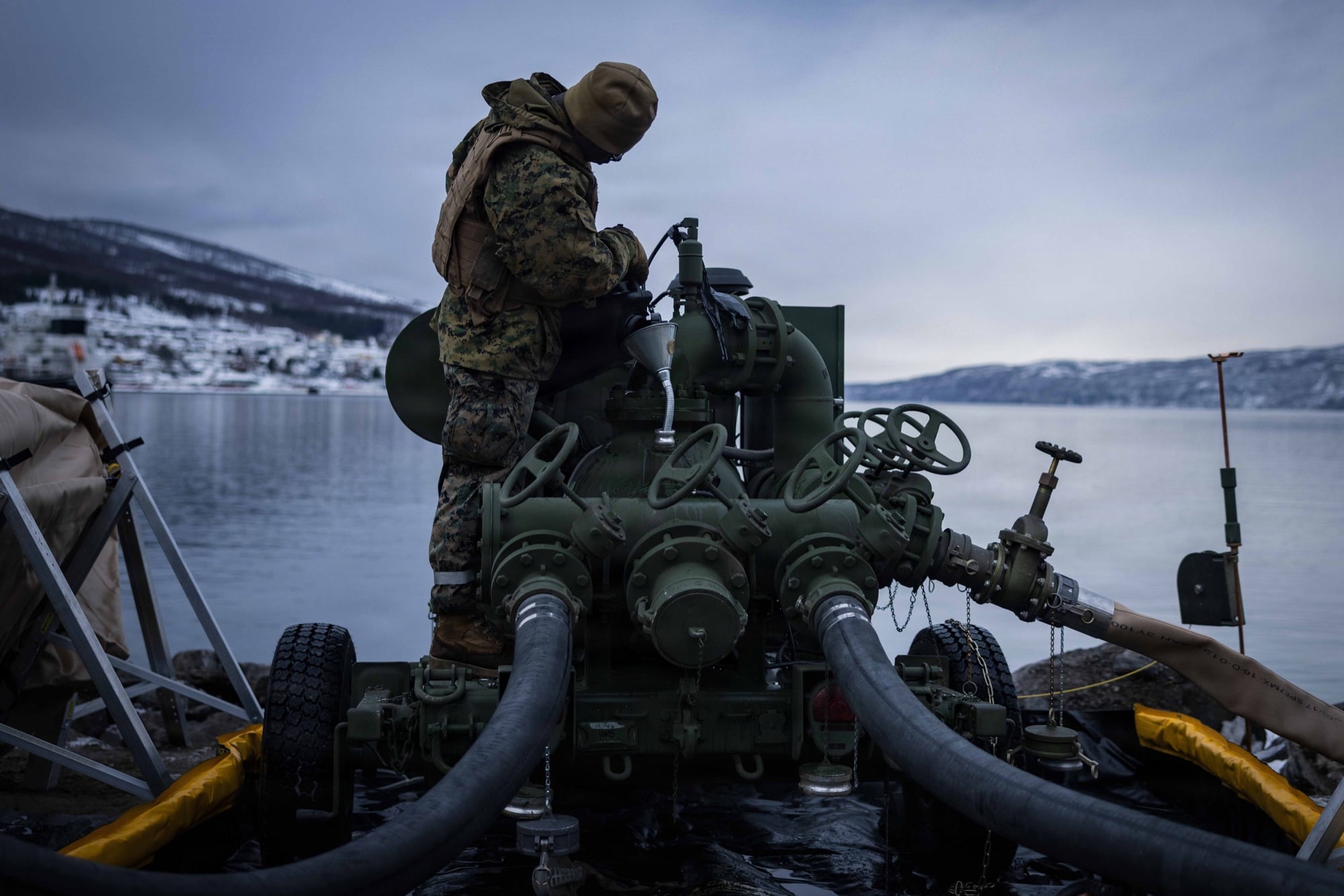 Service member operating fuel-transfer equipment at a snowy waterfront